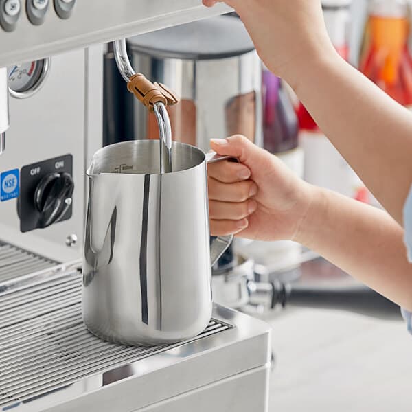 A person pouring milk into a silver Estella Caffe frothing pitcher.