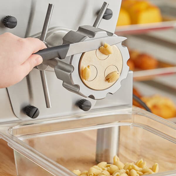 A hand with a black and yellow tool using a machine to cut dough.