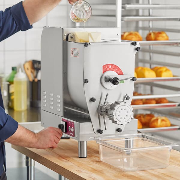 A man pouring liquid into an Estella countertop pasta extruder machine.