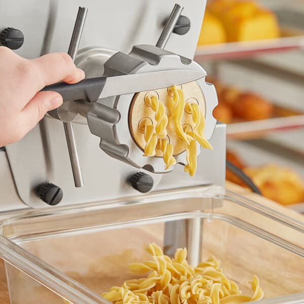 A hand using a black handled pasta machine to cut fusilli noodles.
