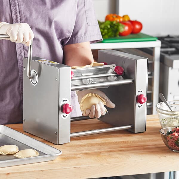 A woman in a purple shirt and gloves using an Estella manual turnover machine to make a semi-circle pie.
