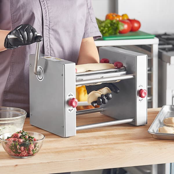 A person wearing black gloves using an Estella Manual Turnover Machine to make meat and spinach dumplings.
