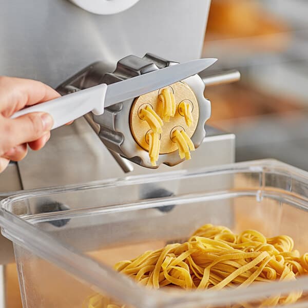 A person using a knife to cut pasta over a container.
