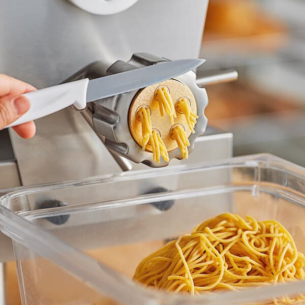 A hand using a knife to cut noodles with an Estella spaghetti pasta die on a pasta machine.