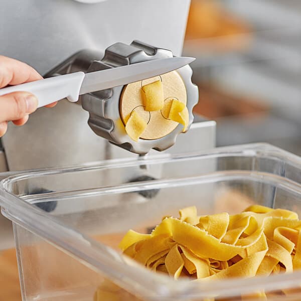 A hand uses a knife to cut pasta on a counter.