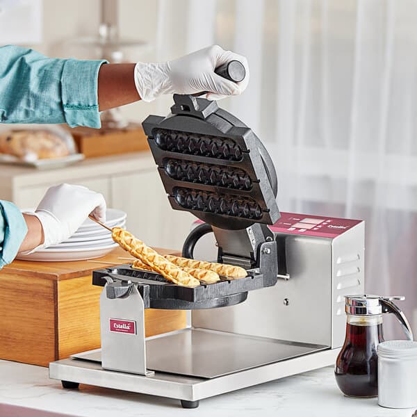 A person using an Estella Belgian waffle maker to make waffles on a stick.