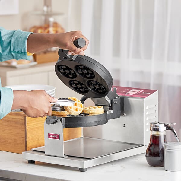 A person using an Estella Belgian Waffle Maker to make mini waffles.