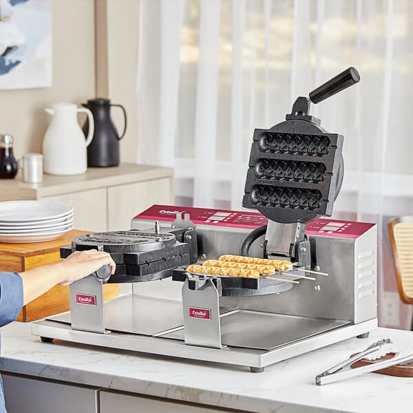 A person using a Estella Double Belgian Waffle Maker to make waffles on a stick.