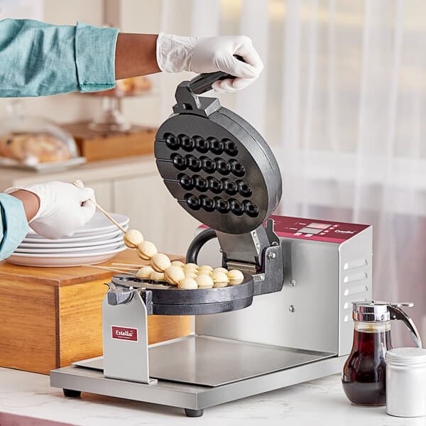 A person using an Estella bubble waffle maker on a counter.