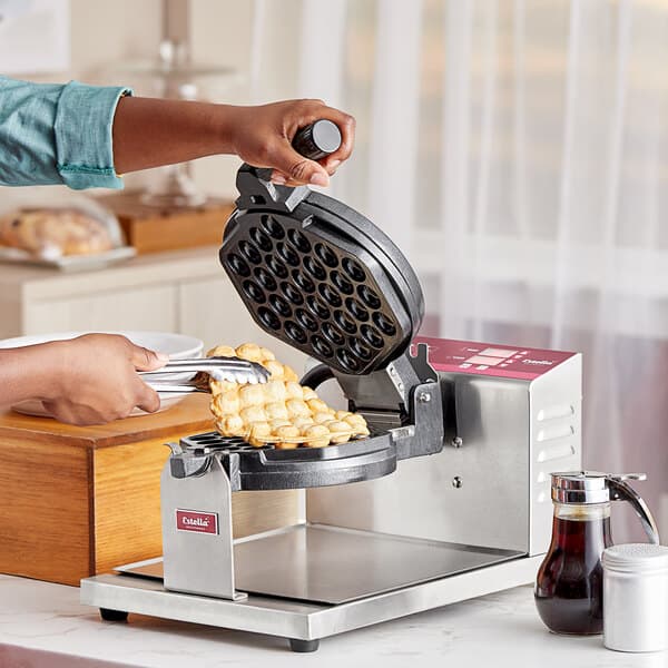 A person using an Estella Belgian waffle maker to make bubble waffles.