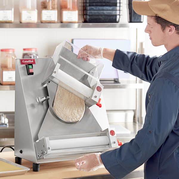 A person in a blue uniform rolling dough into an Estella countertop dough sheeter.