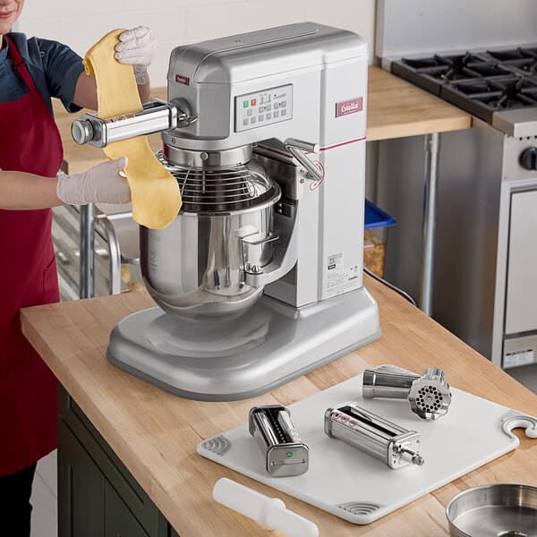 A woman using the Estella meat grinder and pasta roller attachment on a mixer in a kitchen.