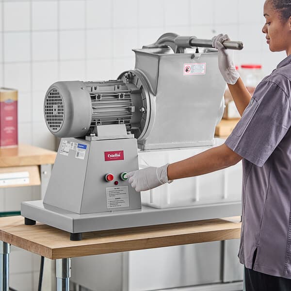 A woman in a grey uniform and gloves using an Estella electric hard cheese grater.