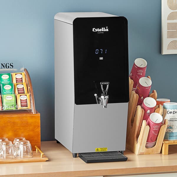 A Estella Caffe tap-operated hot water dispenser on a counter next to a cup of tea.