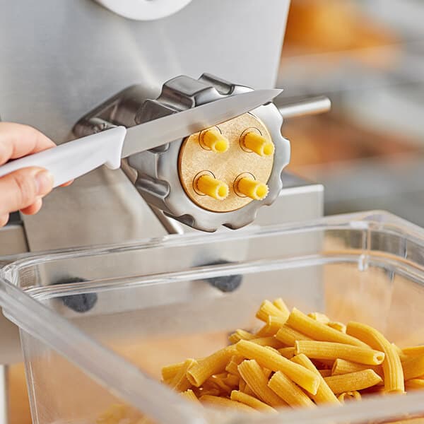 Rigatoni pasta being cut with a knife over a container of pasta.