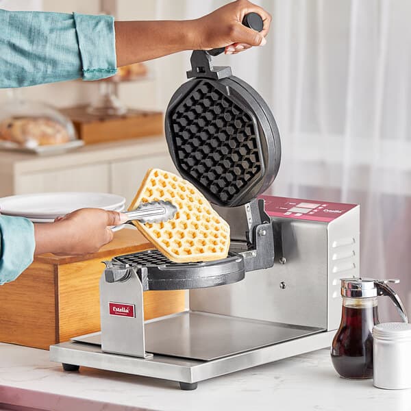 A person making waffles on an Estella Belgian waffle maker with hexagon waffle plates.